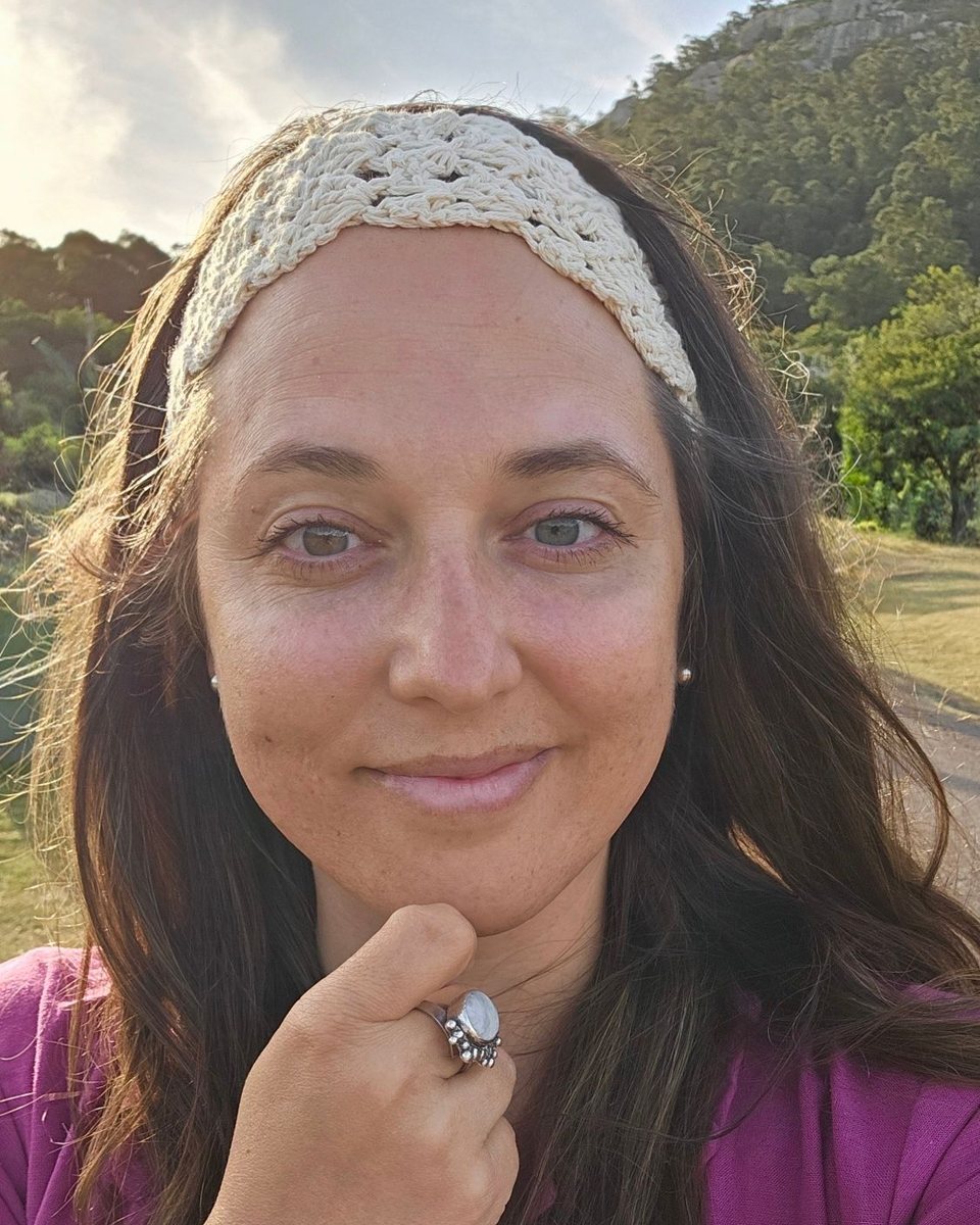 Lorena Odacio Tiozzo sonriendo al aire libre, con vincha tejida y camisa fucsia, con un cerro y vegetación de fondo